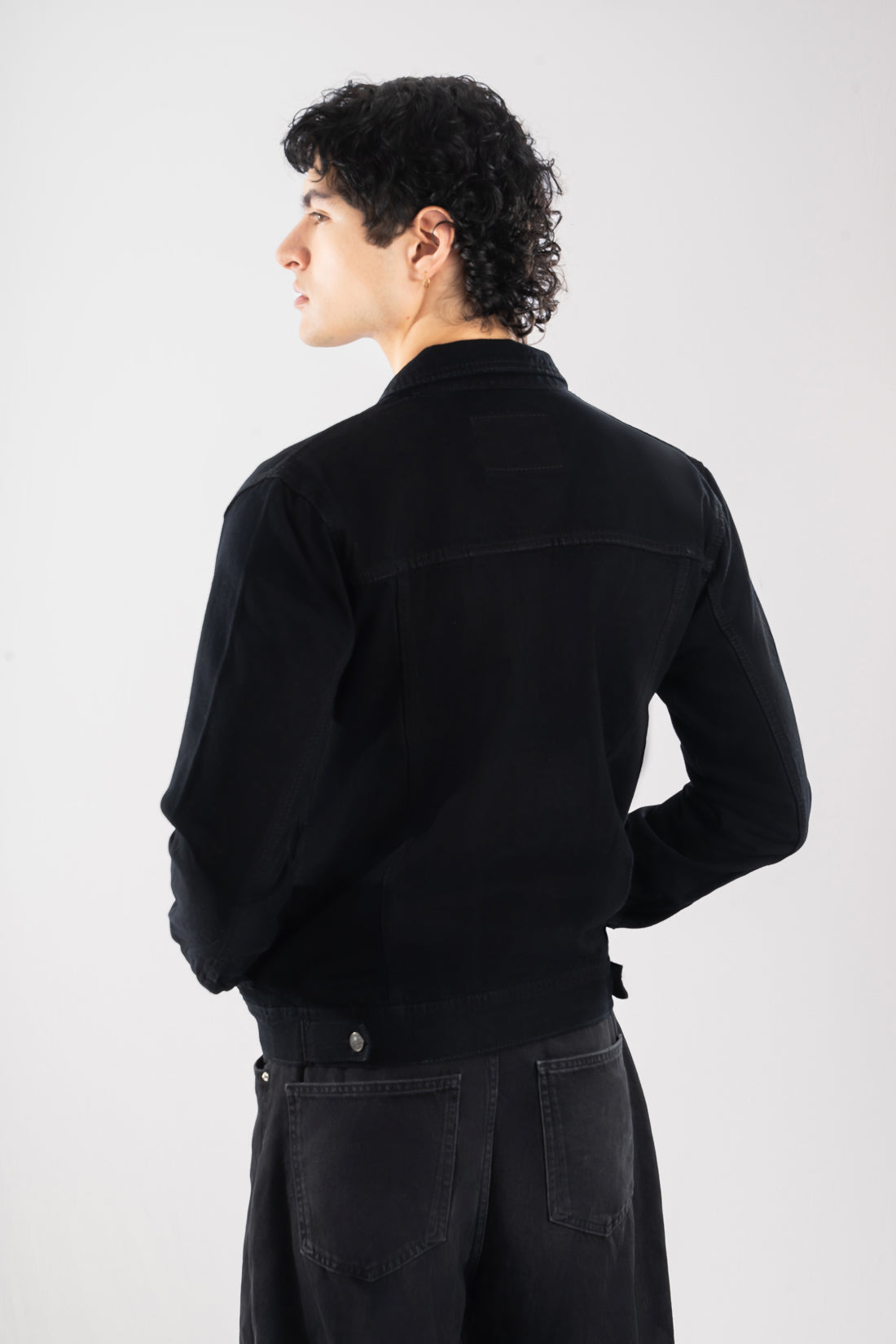 Vista trasera de la chaqueta de jean negra para hombre, mostrando el corte clásico y las correas de ajuste en la cintura.