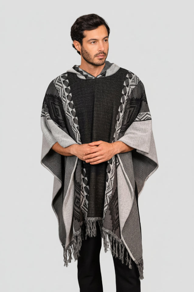 Hombre vistiendo una ruana negra modelo Catalán, con capucha, patrones geométricos (grecas) y flecos artesanales.