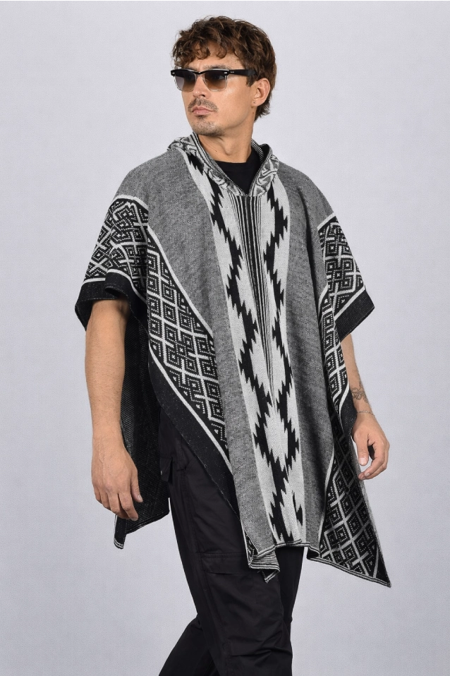 Hombre vistiendo una ruana gris modelo Durango, con capucha, flecos y patrones geométricos (grecas) tejidos.