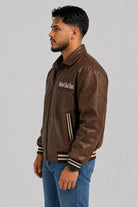 Vista lateral de la chaqueta beisbolera oversize café en cuero sintético con hombro caído