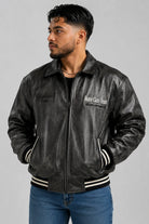 Chaqueta beisbolera oversize gris oscuro cerrada, con resorte negro de rayas blancas en puños y ruedo