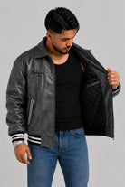 Chaqueta beisbolera gris oscuro abierta mostrando el forro interior acolchado en rombos color negro