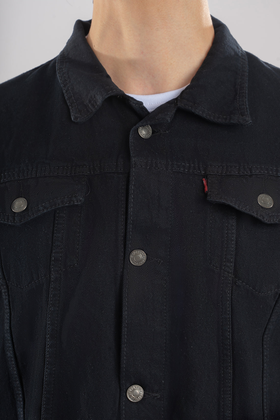 Primer plano del botón metálico grabado y la costura ocre en contraste sobre el denim de una chaqueta de jean negra.