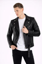 Hombre posando una Chamarra de cuerotex negra para hombre, con un estilo rockero y detalle de correa y hebilla, vista frontal.