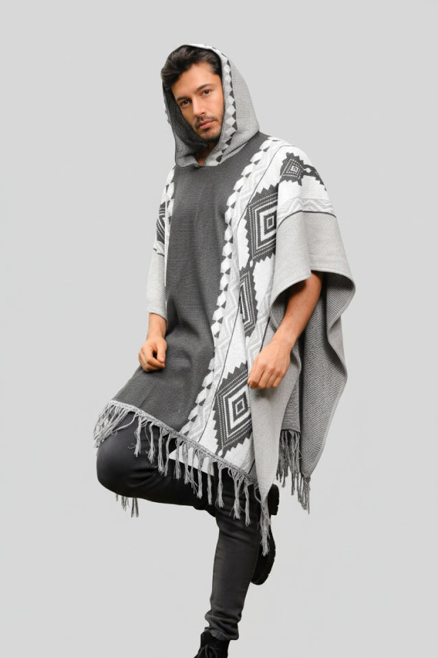 Hombre vistiendo una ruana gris modelo Catalán, con capucha, flecos y patrones geométricos (grecas) tejidos.