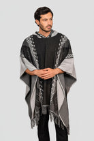Hombre vistiendo una ruana negra modelo Catalán, con capucha, patrones geométricos (grecas) y flecos artesanales.
