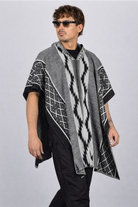 Hombre vistiendo una ruana gris modelo Durango, con capucha, flecos y patrones geométricos (grecas) tejidos.